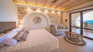 Ein Schlafzimmer mit einem großen Bett, einem Schlafsofa, einem kleinen Tisch und Meerblick durch große Fenster.
