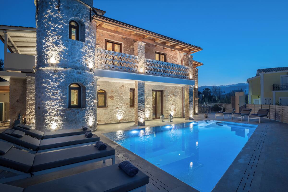 A two-story stone building with a swimming pool, outdoor seating, and a mountain view.