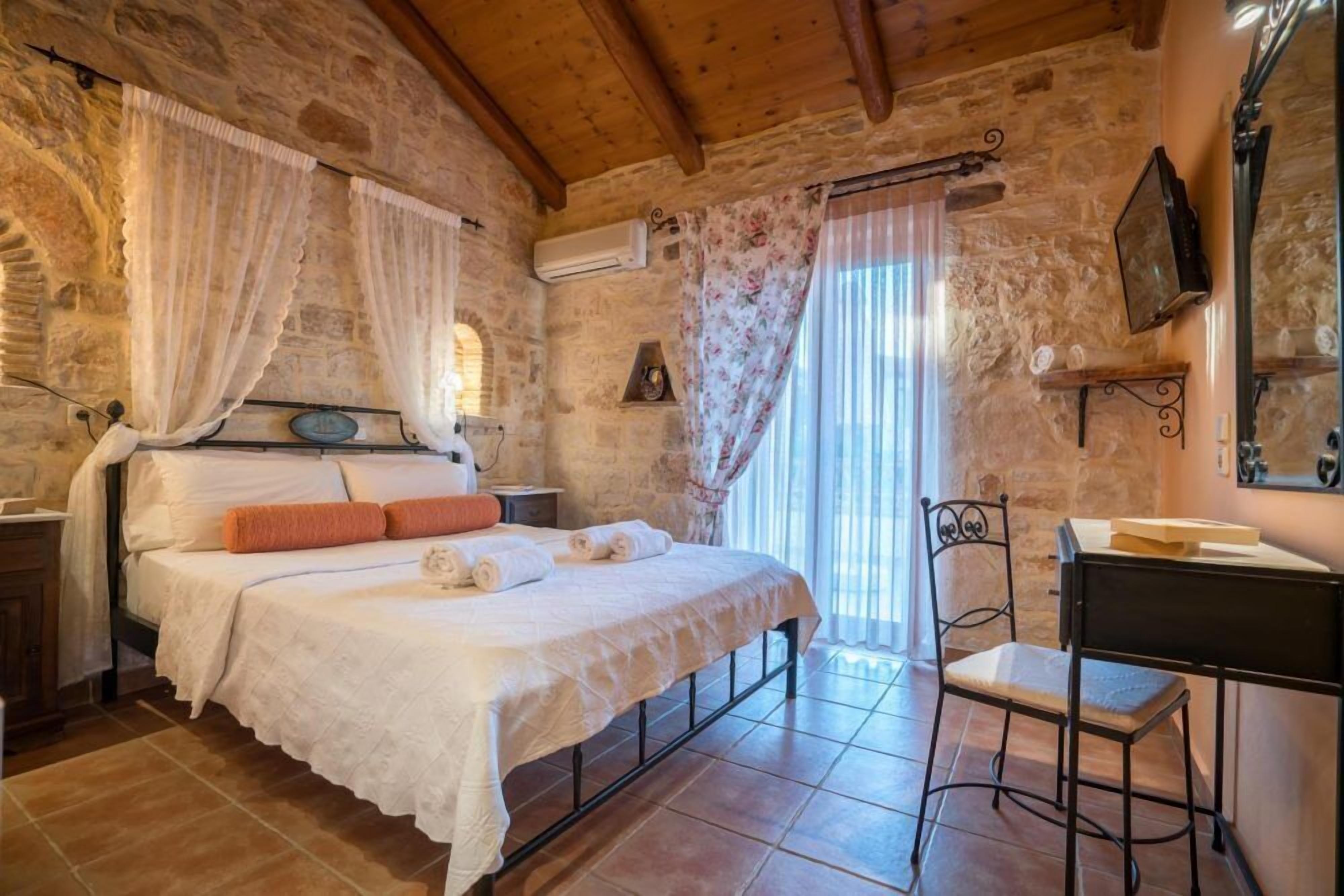 Ein rustikales Schlafzimmer mit Steinwand, einem Bett mit weißer Bettwäsche, einem Holztisch und einem Stuhl.