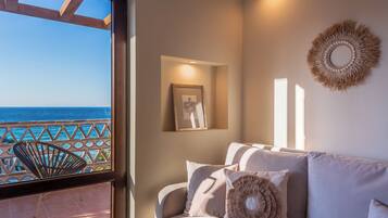 Een balkon met uitzicht op zee, een zithoek met kussens en een lijstfoto, plus decoratieve wandkunst.