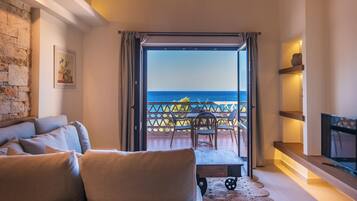 A cozy living room with a sofa, a TV, and a balcony with a view of the sea.