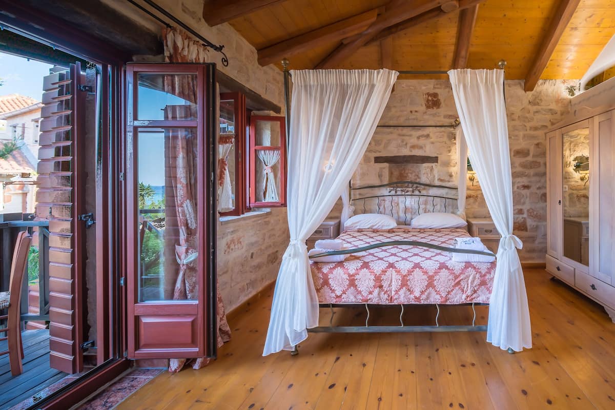 A bedroom with a four-poster bed, a wooden floor, and a stone wall.
