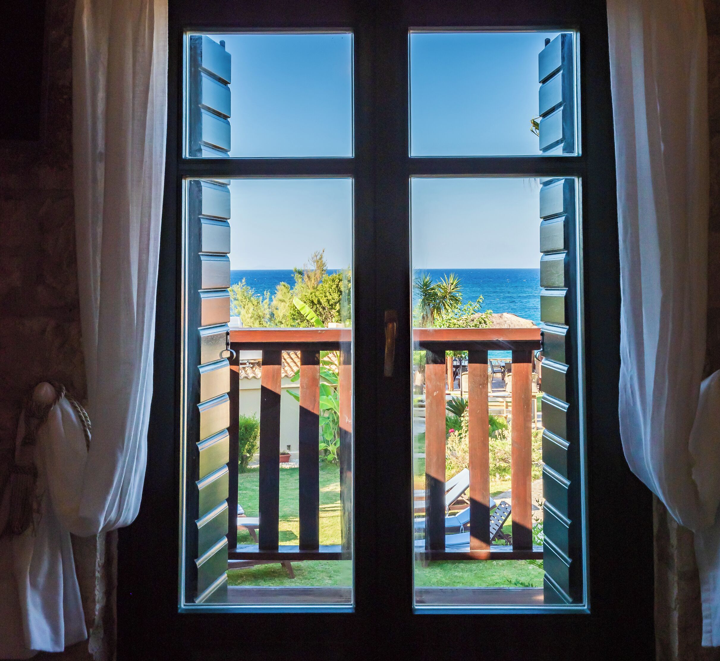 Vista a través de una ventana con balcón, mostrando un cielo despejado y una vista distante del mar.