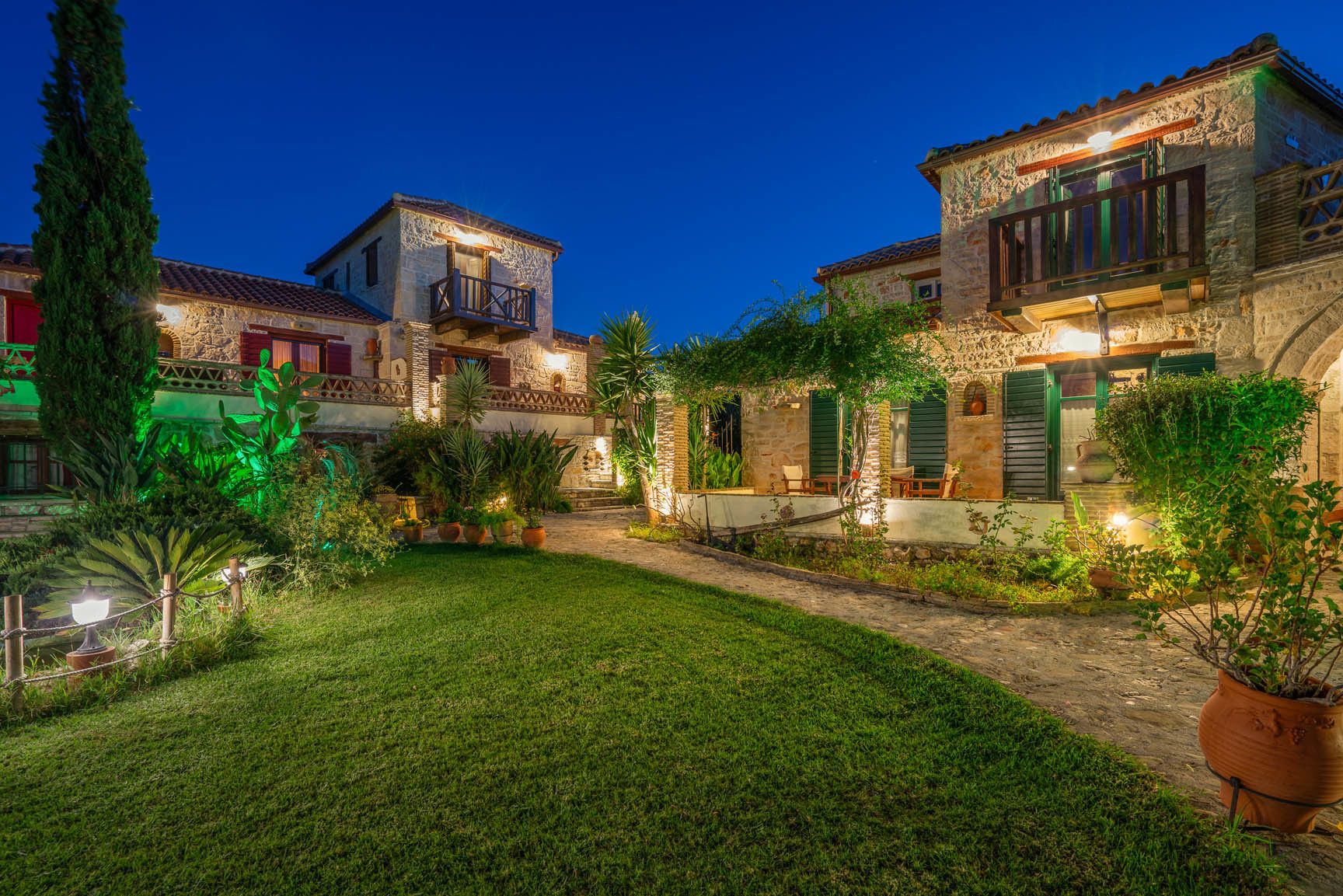A stone building with a balcony, surrounded by a well-maintained garden and potted plants.