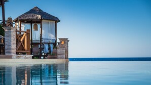 Ein ruhiger Infinity-Pool mit freiem Blick auf den Ozean. Eine hölzerne Laube mit einem Reetdach und einem weißen Baldachin befindet sich neben dem Pool.