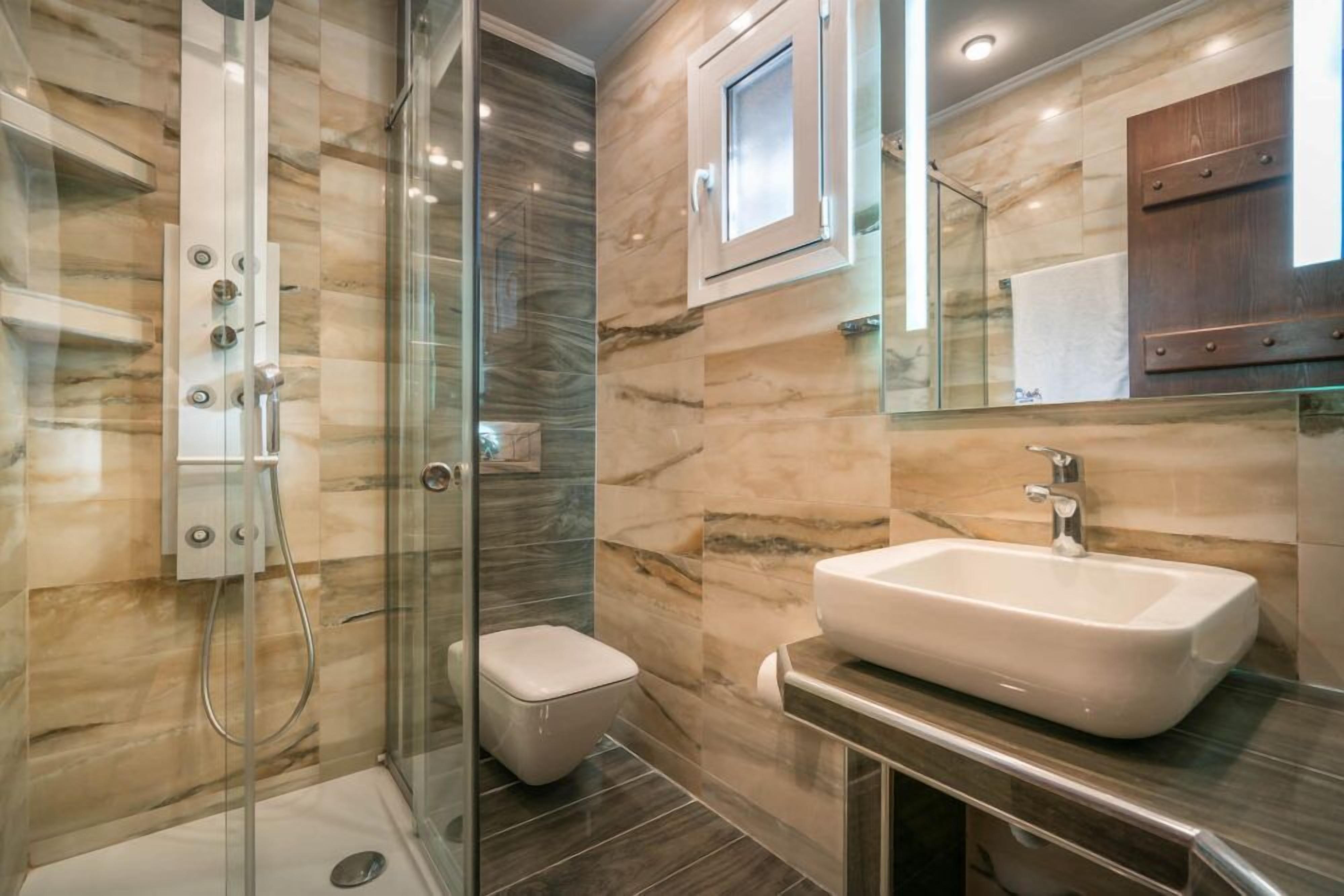 A modern bathroom with a glass-enclosed shower, a white sink, and a marble-tiled wall.