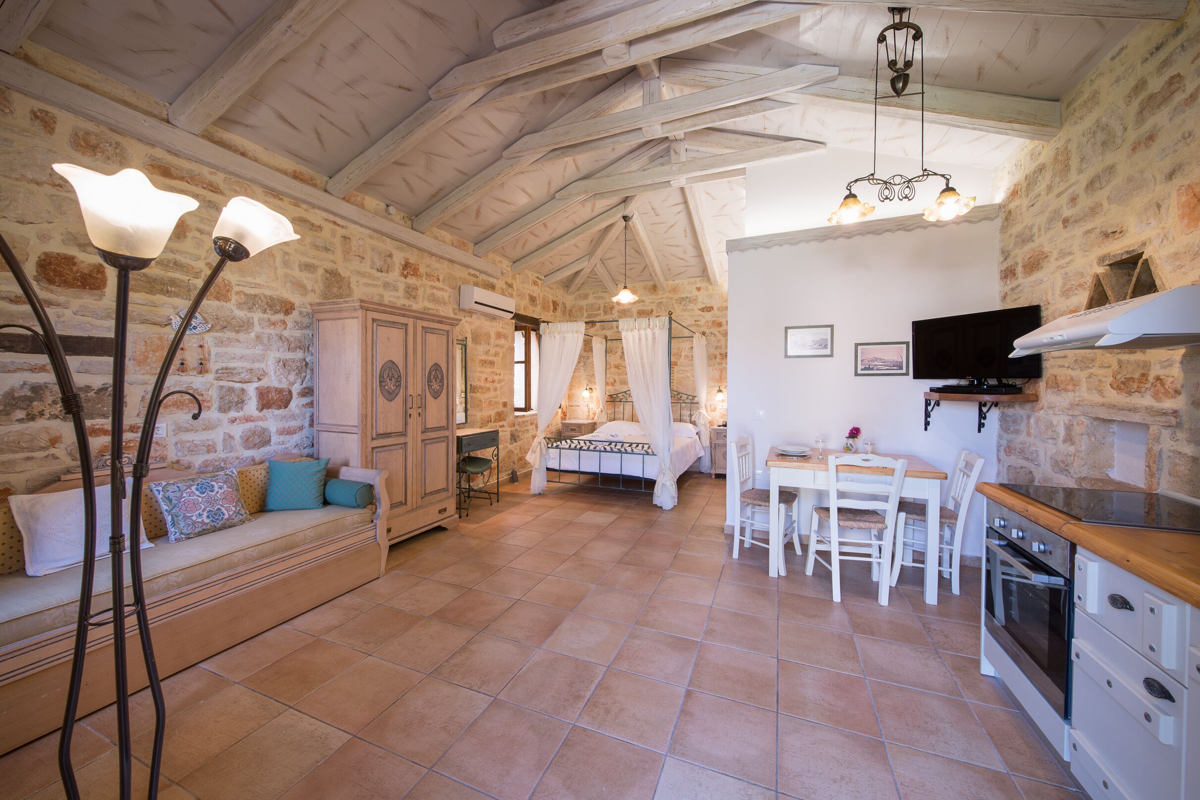 A rustic stone interior with a dining area, kitchen, and a cozy seating area with a sofa and a table.