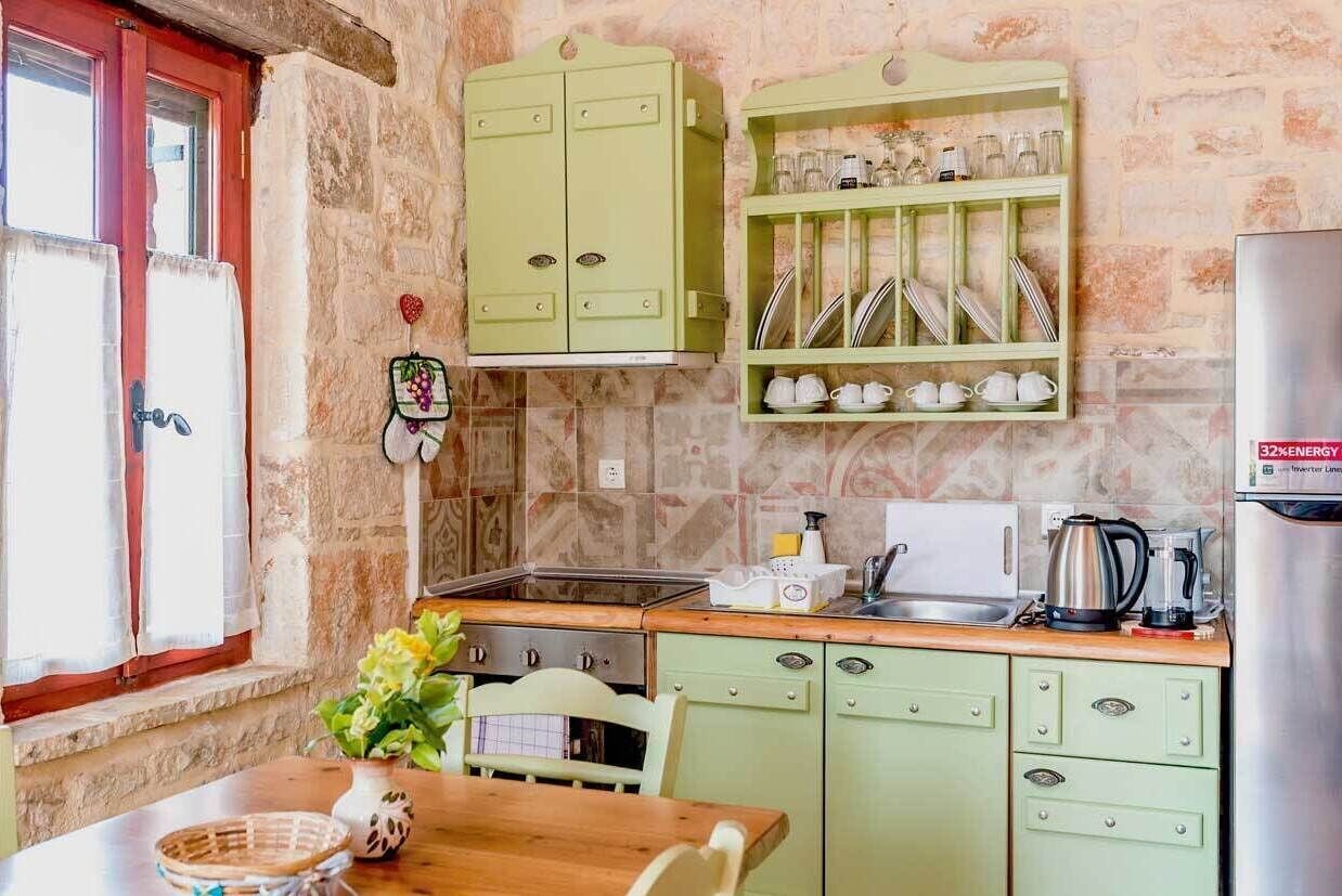 Une cuisine avec des meubles de couleur verte, un pare-feu en carreaux, un réfrigérateur en acier inoxydable et une fenêtre avec des rideaux.