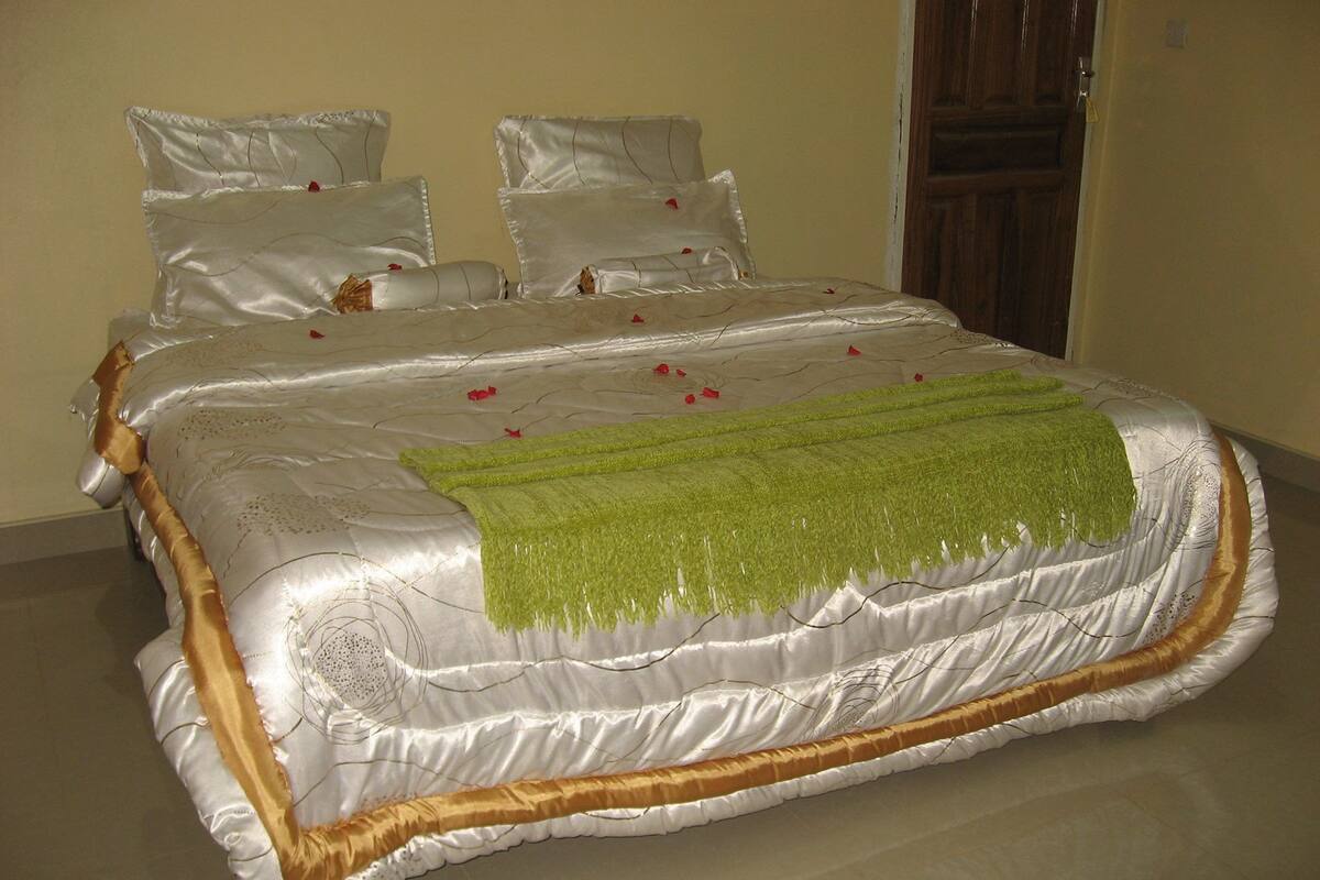 Uma cama bem arrumada com cobertura de cetim, um xale verde e pétalas de rosa espalhadas sobre a cama.