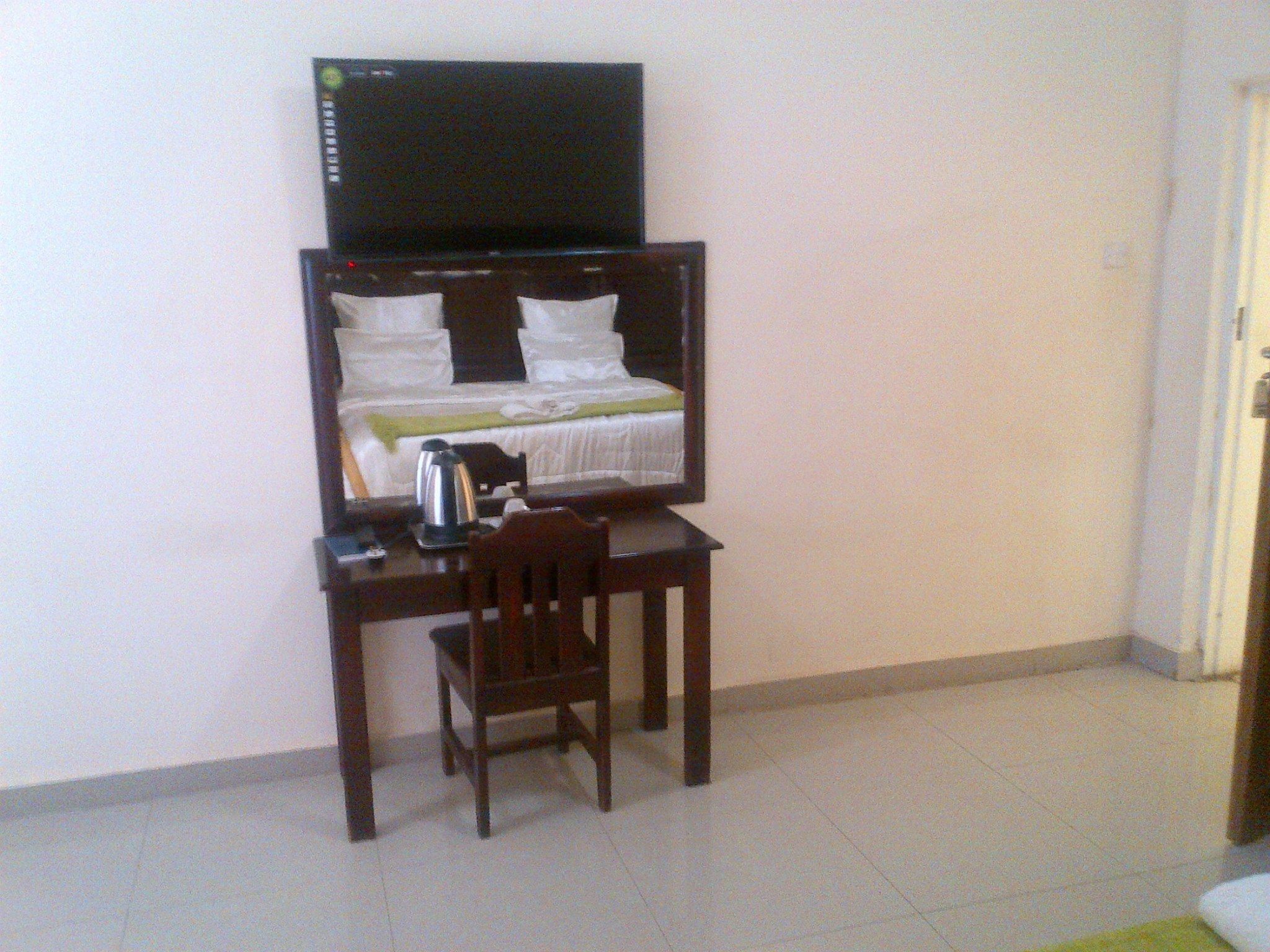 Une petite pièce comprenant un lit, un bureau, une chaise et un téléviseur fixé au mur, au-dessus du lit.