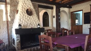 Zona de menjador rústica amb una llar de pedra, cadires de fusta i taula preparada per a una posta.
