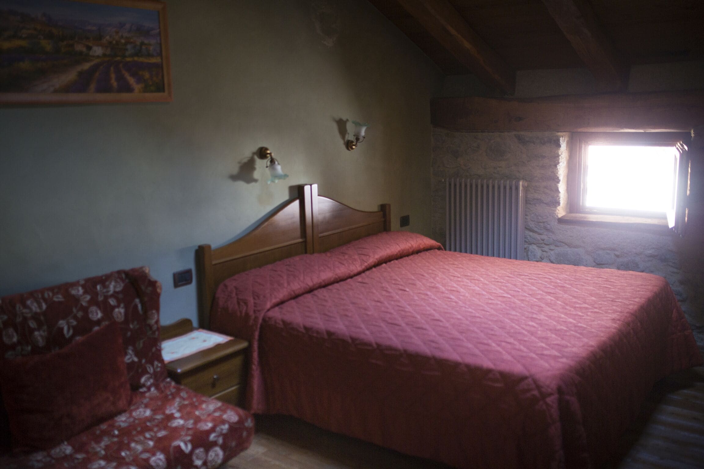 A bedroom with a wooden bed, a nightstand, a floral sofa, and a painting on the wall.