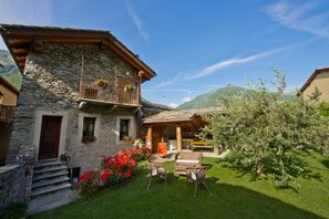 Ein Haus aus Stein mit einem Balkon, einer Holzterrasse und einem Rasen mit Sitzgelegenheiten.