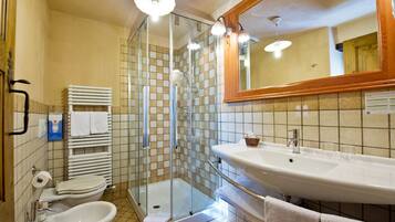 Een badkamer met een douche met glazen wand, een wastafel, een toiletbrons en een toilet.