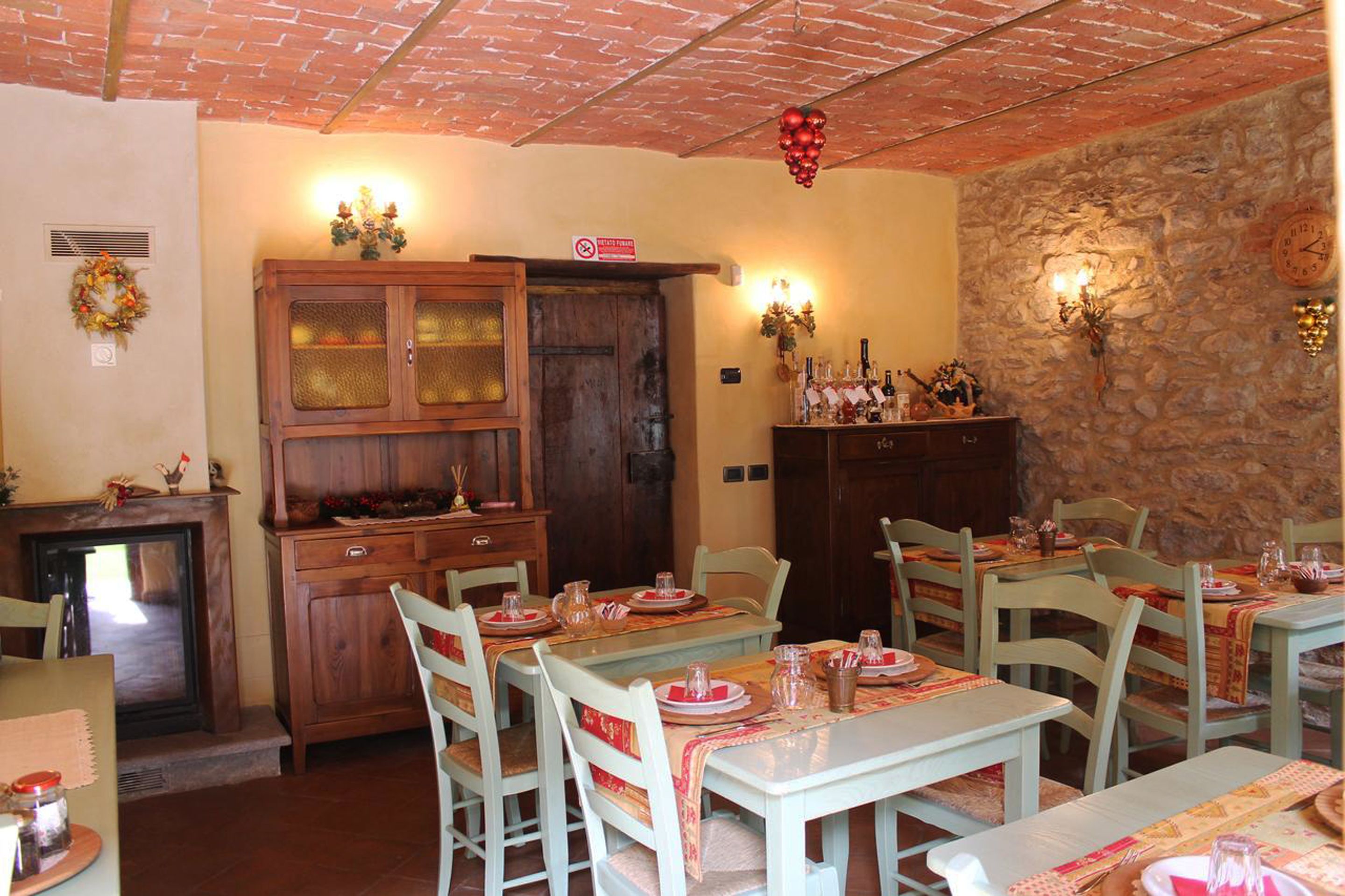 A dining area with wooden tables and chairs, a fireplace, and a stone wall.