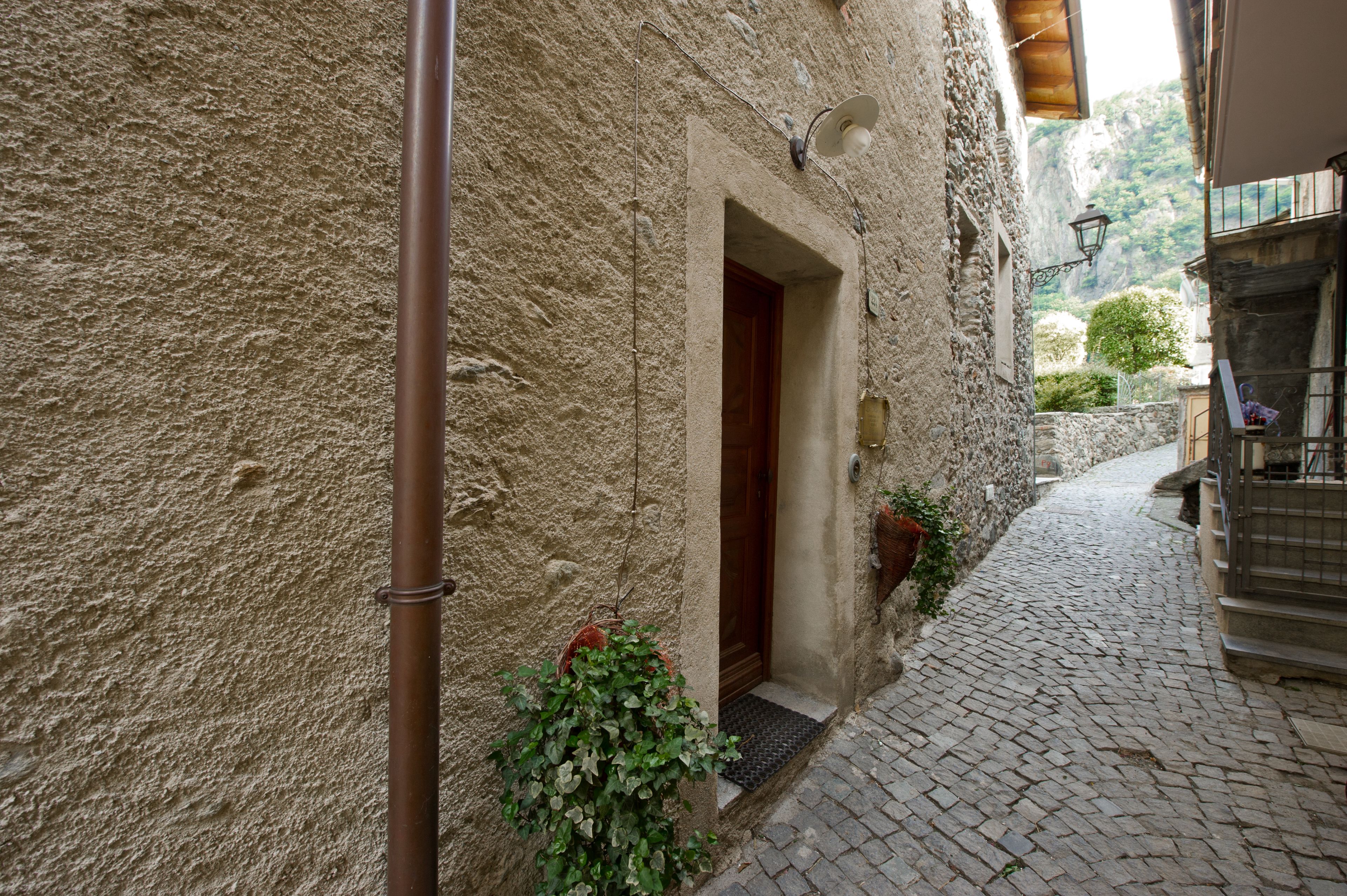 Una estrecha calle adoquinada con un edificio de piedra rústica, una puerta de madera y una planta colgante.