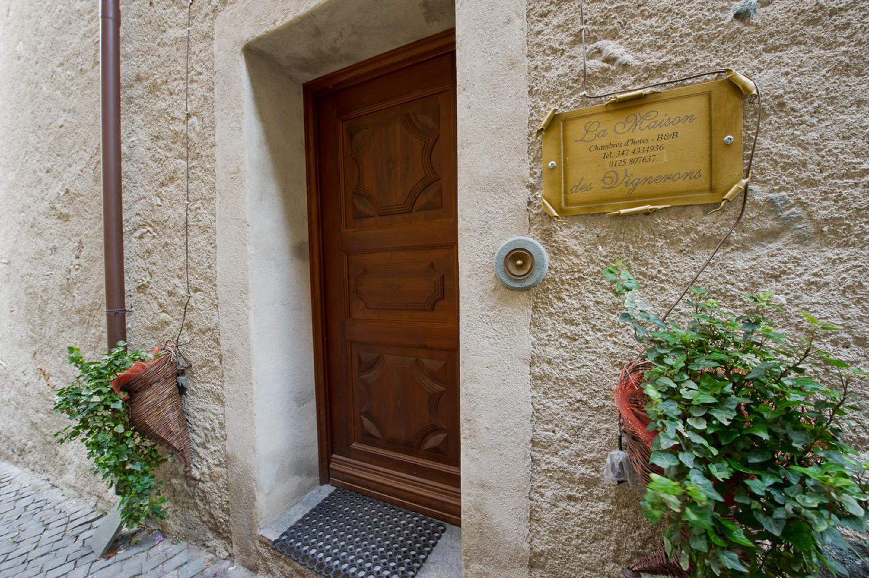 A stone building with a wooden door, a metal plaque, and potted plants.