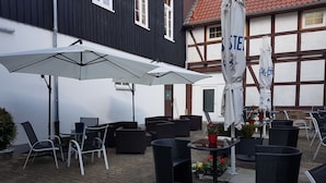 An outdoor patio area with wicker furniture, umbrellas, and potted plants. - Ratskeller Nörten (Norten-Hardenberg)