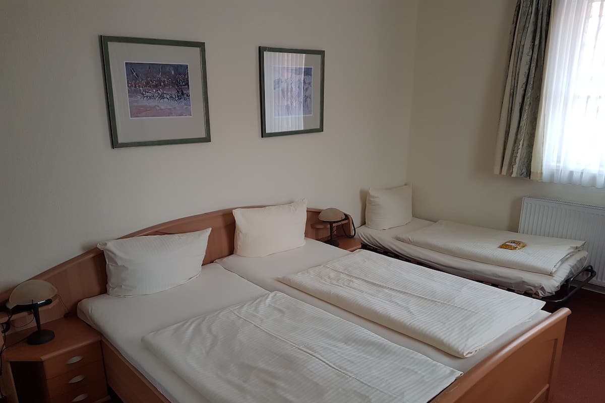 Ein Hotelzimmer mit zwei Einzelbetten, einem hölzernen Kopfteil, einem Nachttisch mit Lampe sowie zwei gerahmten Bildern an der Wand.