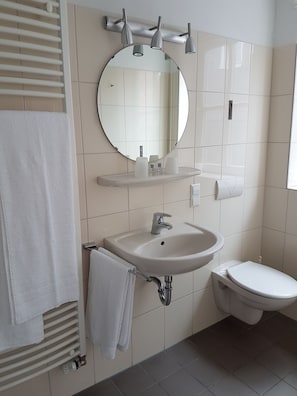 A bathroom with a white sink, a toilet, a towel rack, a mirror, and a towel hanging on the rack. - Ratskeller Nörten (Norten-Hardenberg)