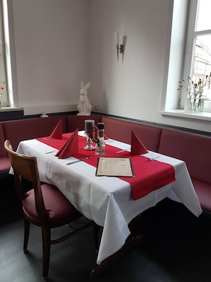 A dining area with a table set for two, a red cushion, a menu, and a salt and pepper shaker. - Ratskeller Nörten (Norten-Hardenberg)