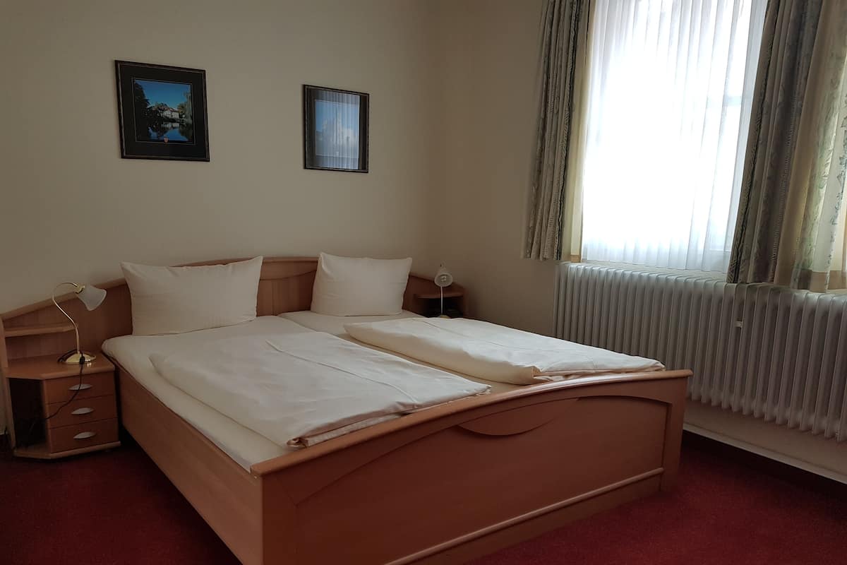 Ein Doppelbett mit Holz-Kopfteil, zwei Nachttische mit Lampen, eine Heizung und zwei gerahmte Bilder an der Wand.