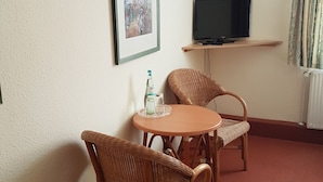 A room with a television on a shelf, two wicker chairs around a small table, and a framed picture on the wall. - Ratskeller Nörten (Norten-Hardenberg)