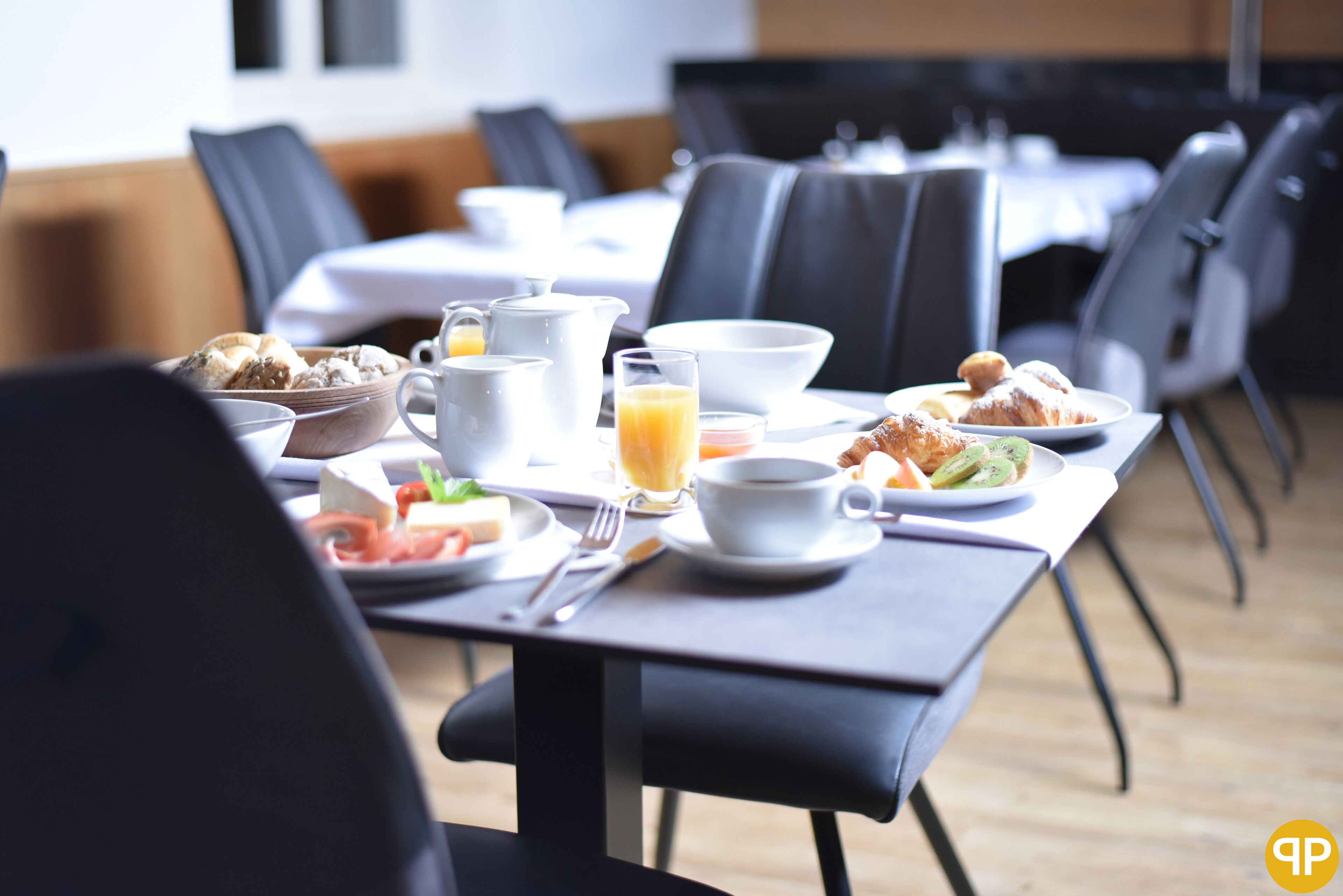 A breakfast setting with a table set for two, including plates of food, a coffee pot, and a glass of orange juice.