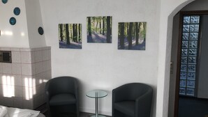A room with a fireplace, two armchairs, a small glass table, and three forest-themed paintings on the wall. - Gästehaus Birke (Titisee-Neustadt)