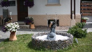 A stone fountain with a sculpture in the center, surrounded by potted plants and a building with a beige and white facade. - Gästehaus Birke (Titisee-Neustadt)