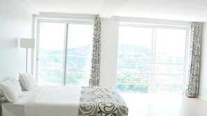 Un dormitorio con una cama grande, dos ventanas y vistas a un paisaje urbano.