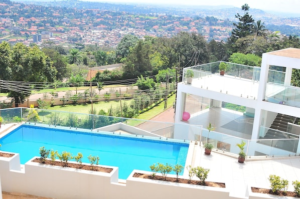 A modern house with a large swimming pool, a second-floor balcony, and a view of a cityscape.