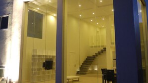 Un edificio moderno con fachada de vidrio, una escalera y un área de descanso visible a través del cristal.
