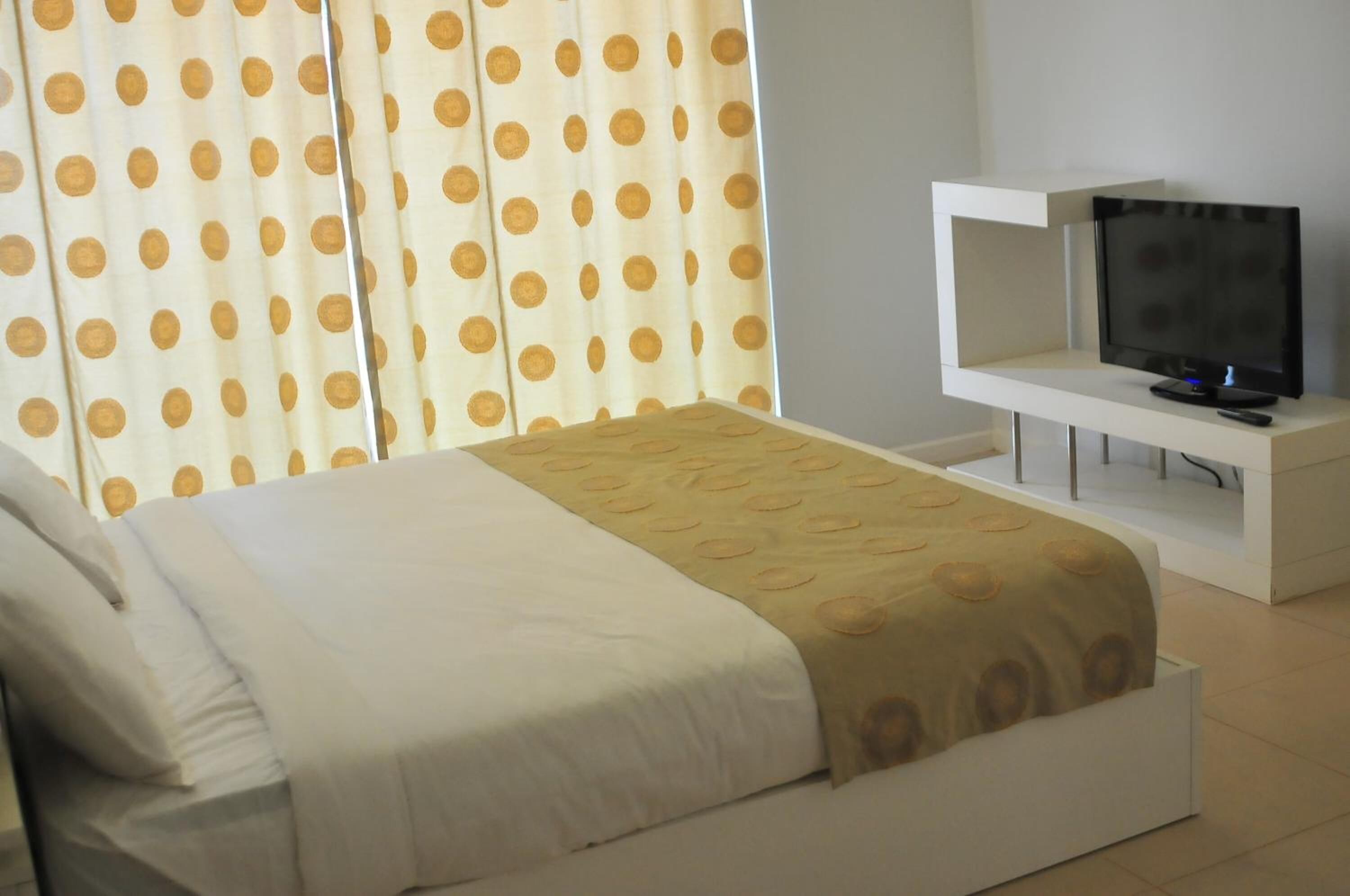 A hotel room with a bed, a TV on a stand, and curtains with a polka dot pattern.