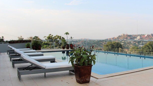 Piscina en la azotea con sillones de descanso y plantas en macetas, con vistas a un paisaje urbano.