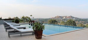 A rooftop pool with lounge chairs and potted plants, overlooking a cityscape. - The Seventeen Apartment Hotel (Kampala)