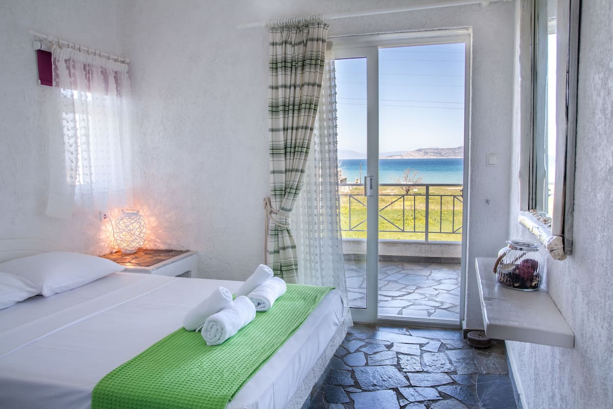 Un dormitorio con cama, una mesita de noche, una manta verde, una ventana con cortinas y vista al mar.