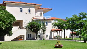 A two-story building with a red-tiled roof, a covered patio area, and a well-maintained lawn with a flower bed. - Phoenix Beachside Condos (Velo-Vocha)