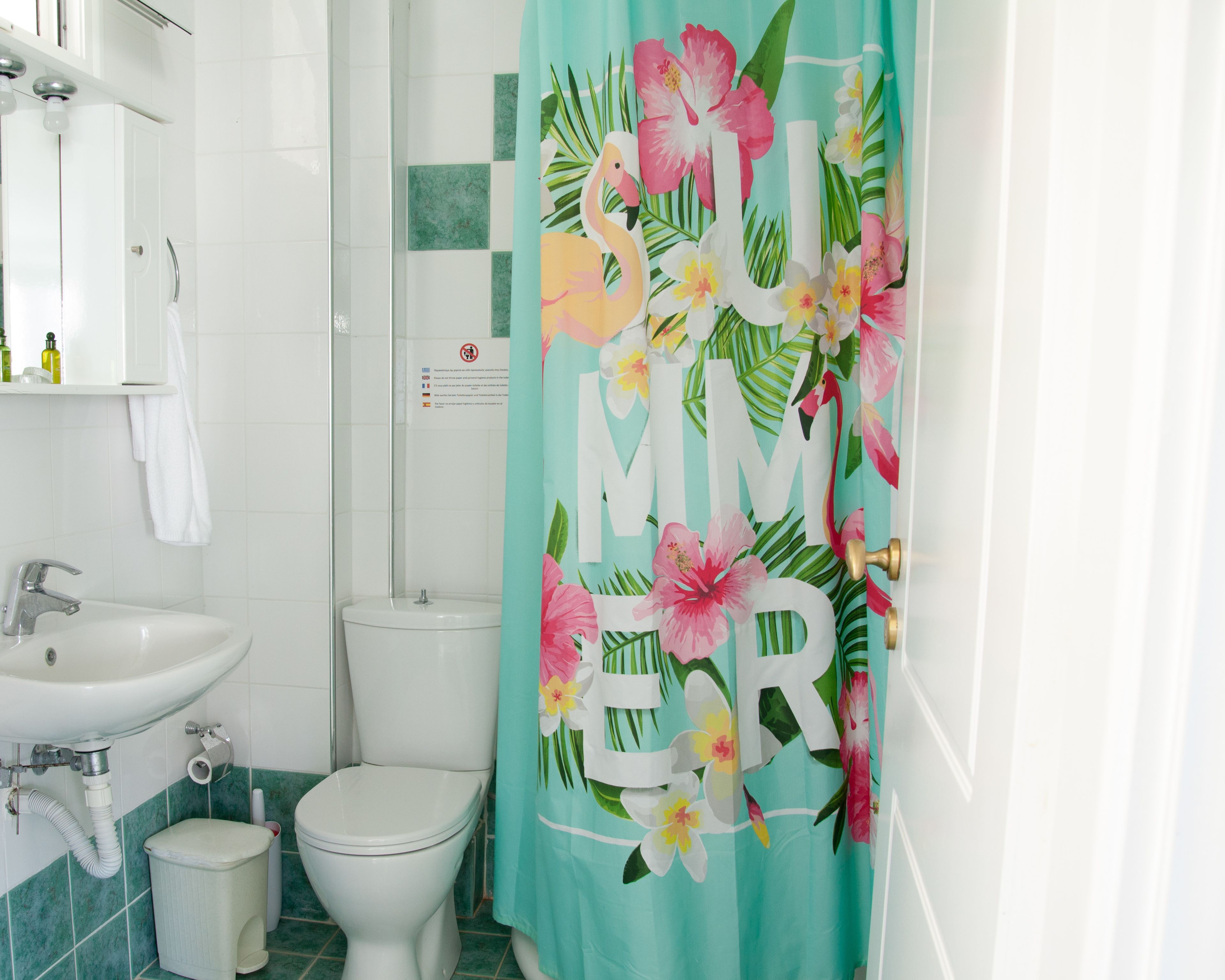A bathroom with a white sink, toilet, and shower curtain with a tropical print.
