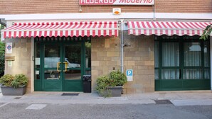 Un edificio con toldo a rayas rojas y blancas, un letrero que dice 'ALBERGO Moderno' y una señal de estacionamiento.