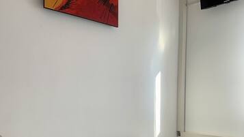 A hotel room with a bed, a painting on the wall, and a TV mounted on the wall.
