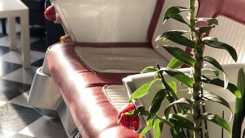 Ein Zimmer mit kariertem Boden, einem roten Ledersofa, einer Zimmerpflanze und einem kleinen Tisch mit einem rosafarbenen Band.