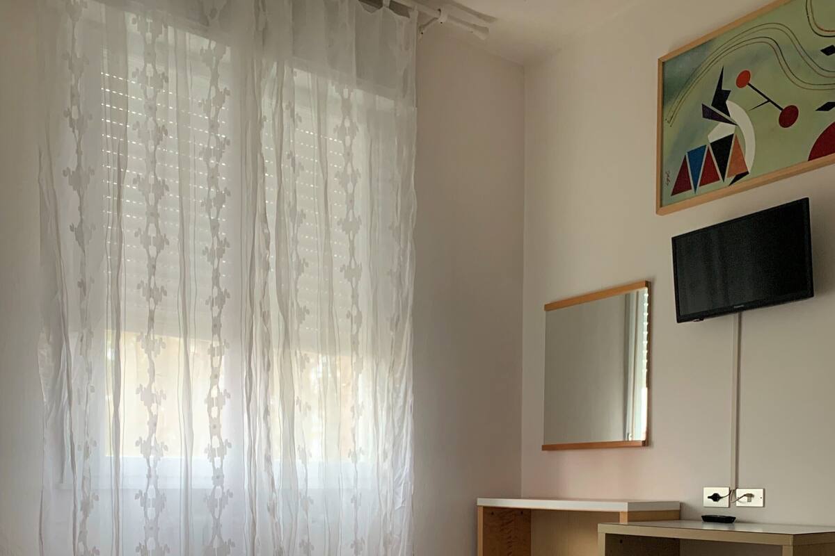 Et hotelværelse med to senge, et fjernsyn, et spejl og et skrivebord.