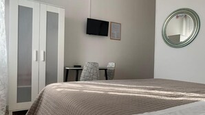 Un dormitorio con cama, armario, escritorio, silla, televisor y espejo.