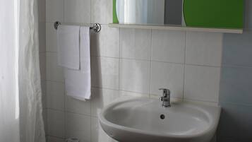 Een badkamer met toilet, bidet, wastafel en een spiegel met een groen plankje erboven.