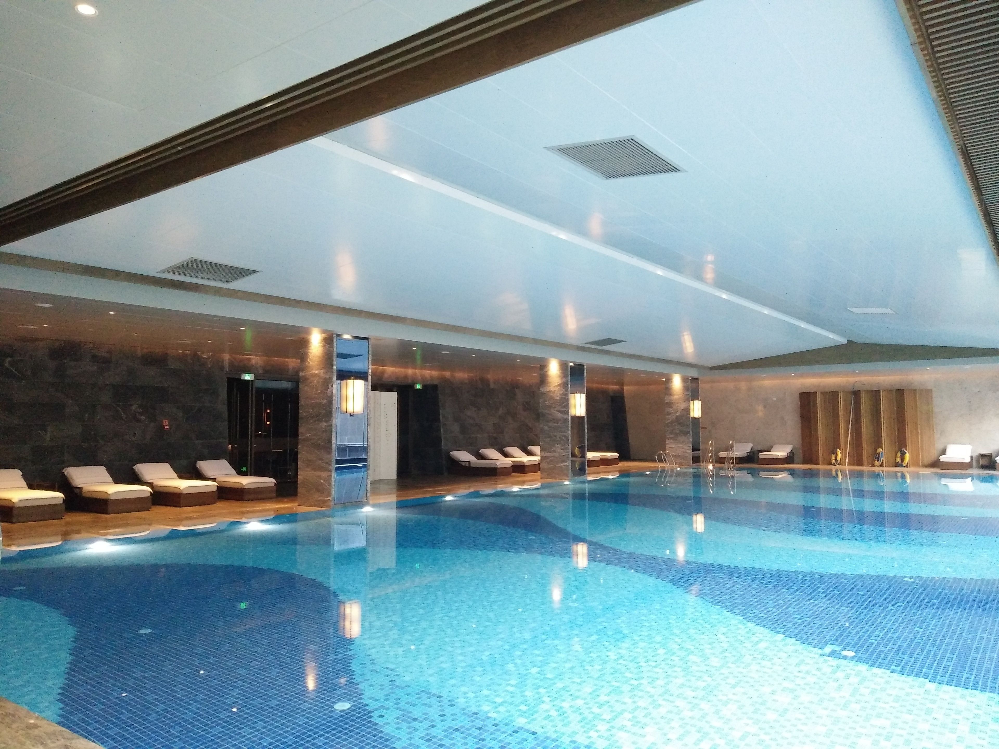 A large indoor swimming pool with lounge chairs and a stone wall.