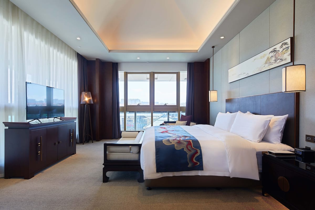 A hotel room with a large bed, a TV, a desk, and a view of the city.