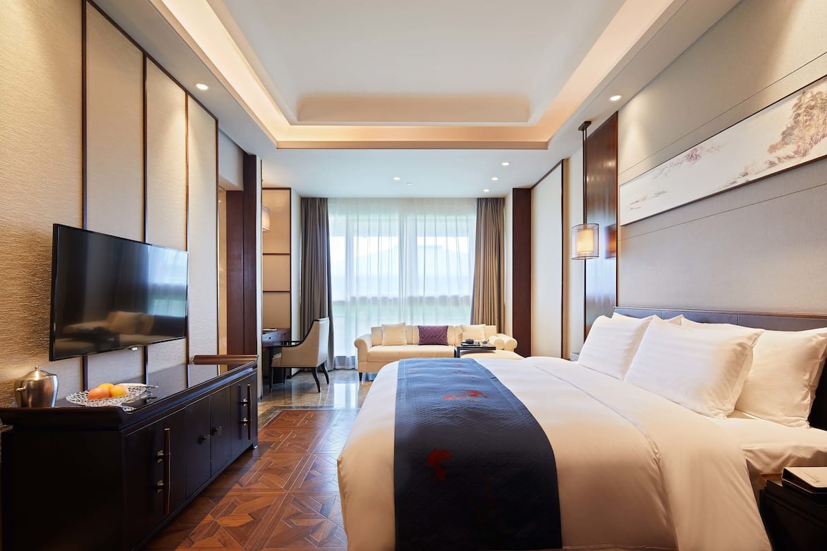 A hotel room with a large bed, a flat-screen TV, a desk with a chair, and a sofa.