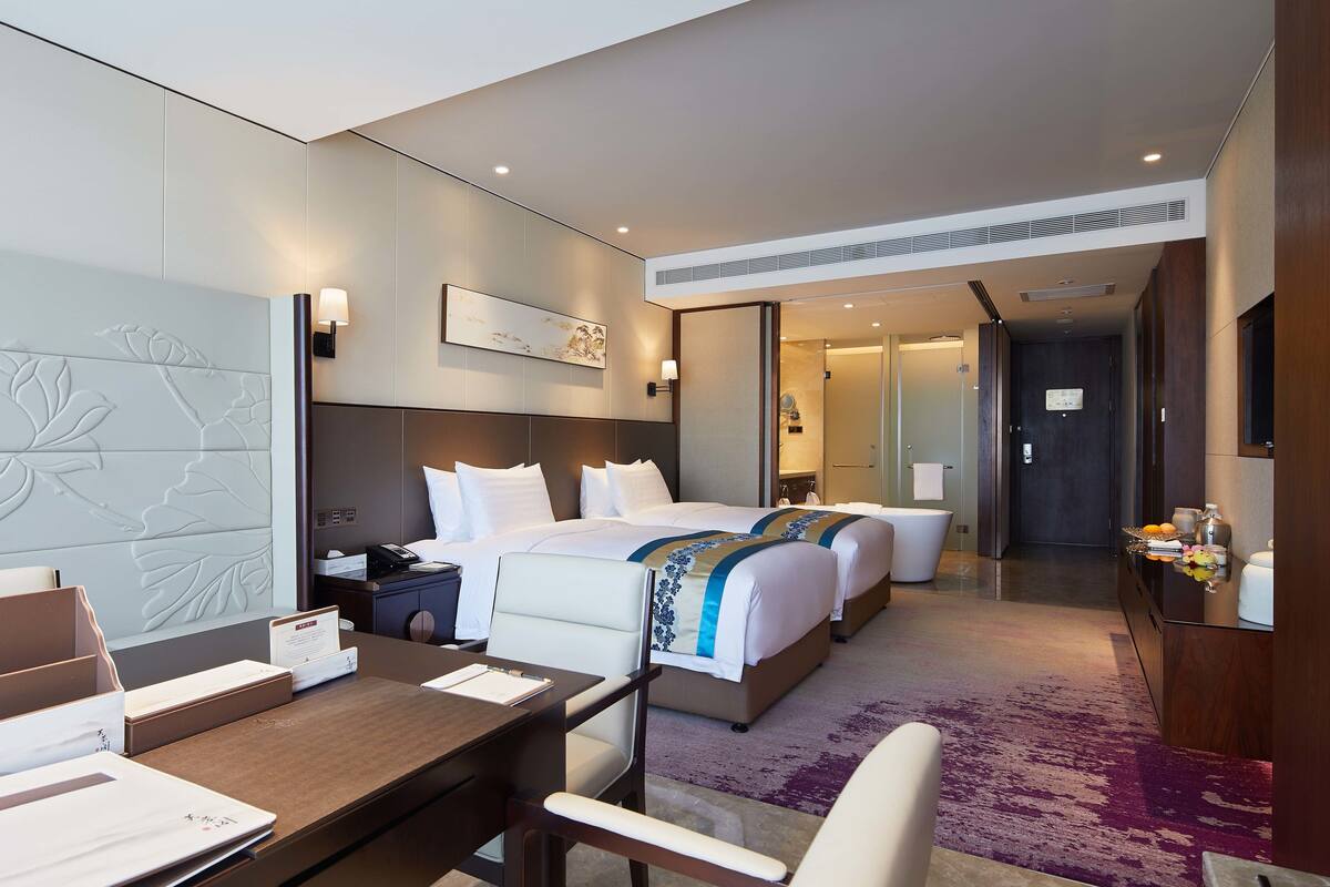 A hotel room with a large bed, a desk with a chair, a bedside table, and a bathroom visible through an open door.