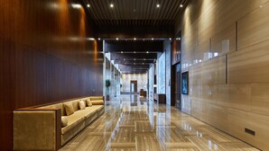 Un moderno vestíbulo de hotel con un largo pasillo, un área de descanso con un sofá y un piso de mármol pulido.